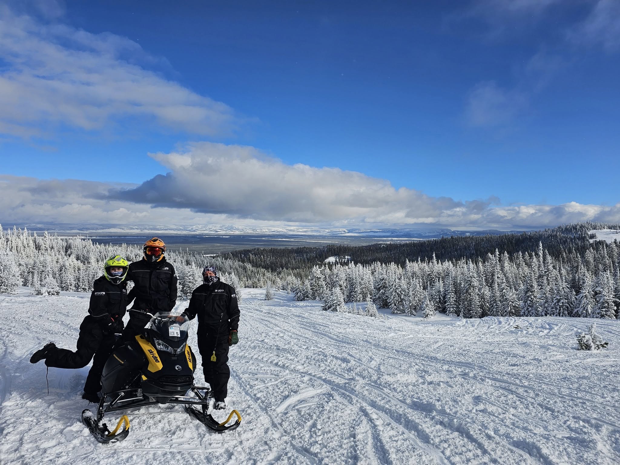 Snowmobilers riding through deep snow in the Montana backcountry with mountain peaks