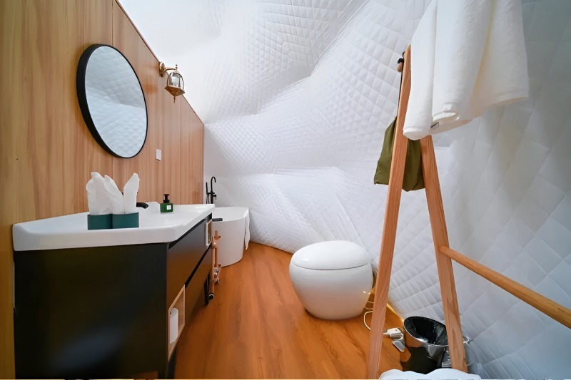 Interior of a glamping dome bathroom featuring curved white quilted walls and ceiling with warm wood-tone paneling.