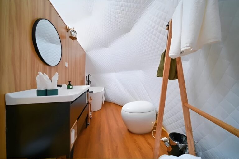 Modern glamping dome bathroom interior with curved white quilted ceiling and walls, wood flooring, and wood-paneled accent wall.