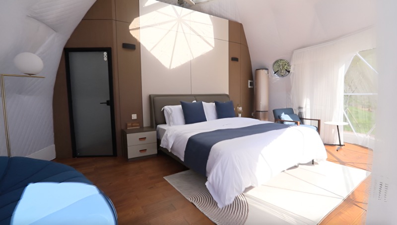 Interior of a modern geodesic dome bedroom with curved white walls, brown accent panels, and contemporary pendant light.